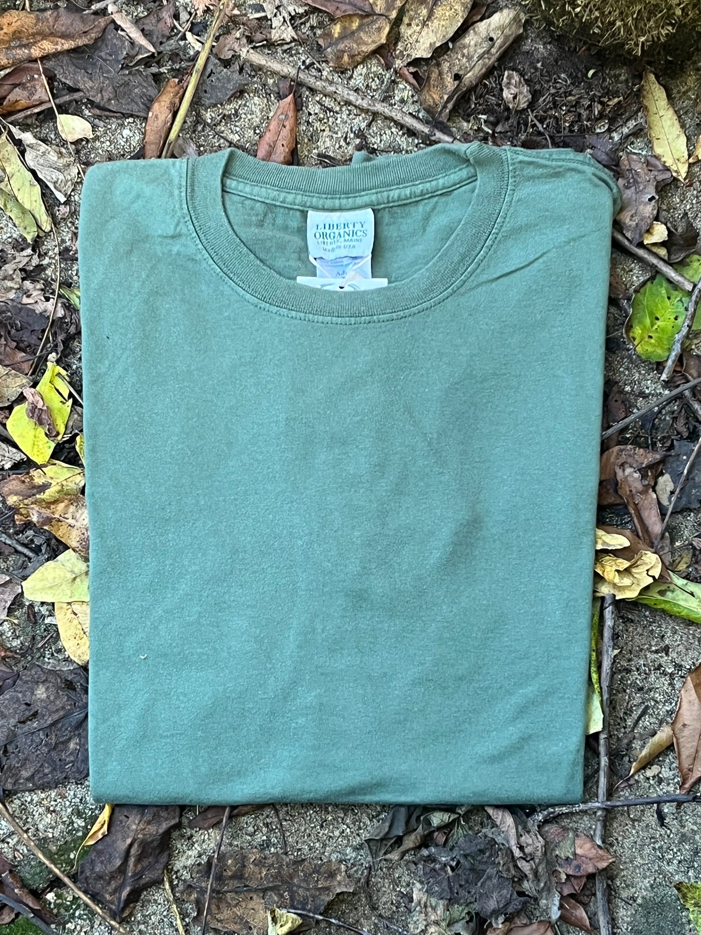 Organic cotton Green t-shirt on a ground surface with leaves and twigs
