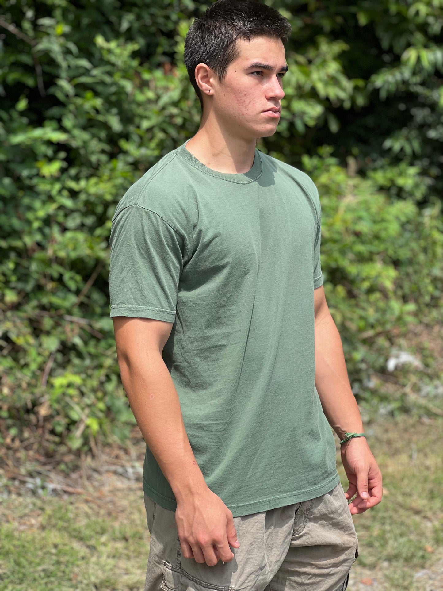 Man wearing a green t-shirt standing outdoors with greenery in the background