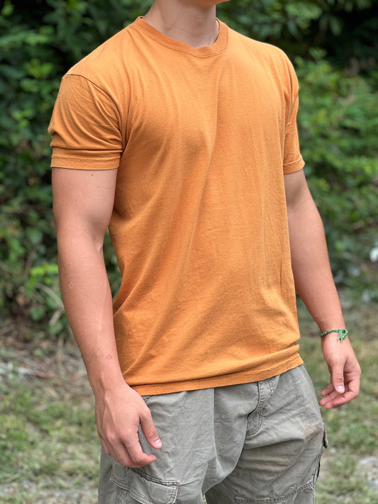 Person wearing a gold colored t-shirt and light gray pants outdoors.
